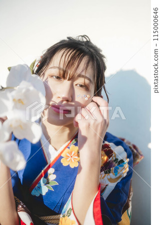 A young woman in a blue kimono holding a white flower 115000646