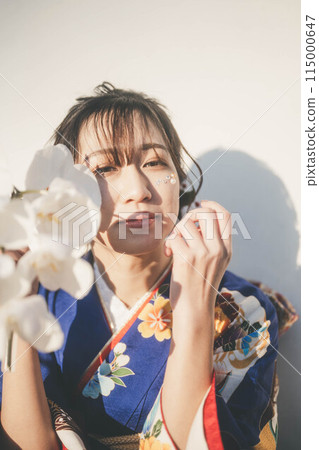 A young woman in a blue kimono holding a white flower 115000647