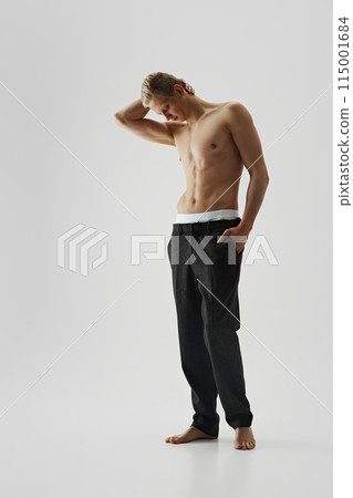 Handsome young man in black pants posing shirtless isolated on grey studio background. Muscular athletic body shape Handsome young man in black pants posing shirtless isolated on grey studio background. Muscular athletic body shape 115001684