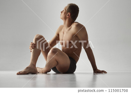 Young bode guy sitting in underwear shirtless with thoughtful expression isolated on grey studio background. Young bode guy sitting in underwear shirtless with thoughtful expression isolated on grey studio background. 115001708