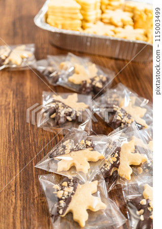 Carefully packaging Christmas cutout cookies, half-dipped in chocolate and presented in clear cellophane wrapping, perfect for festive gifting. Carefully packaging Christmas cutout cookies, half-dipped in chocolate and presented in clear cellophane wrapping, perfect for festive gifting. 115003499