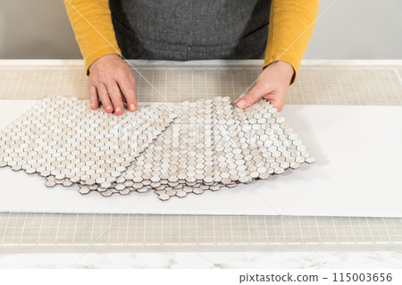 In the process of mounting peel and stick mosaic tiles onto a foam board, perfect for enhancing a food photography studio's aesthetic. 115003656