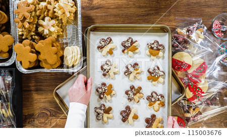 Flat lay. Carefully packaging Christmas cutout cookies, half-dipped in chocolate, sprinkled with crushed nuts, and presented in clear cellophane wrapping. Flat lay. Carefully packaging Christmas cutout cookies, half-dipped in chocolate, sprinkled with crushed nuts, and presented in clear cellophane wrapping. 115003676