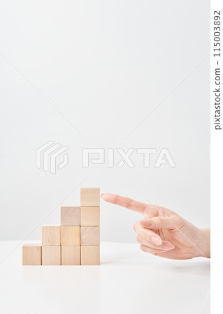 Wooden building blocks stacked in a staircase shape and a woman pointing at them 115003892