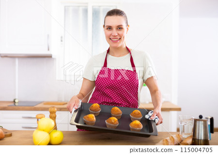 Woman taking out just baked cupcakes. Woman cooking cakes at home 115004705