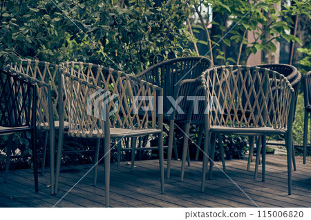 Wicker plastic chairs outdoors, against a background of green bushes. The cafe is closed, there are no visitors in the early morning. With space to copy. High quality photo Wicker plastic chairs outdoors, against a background of green bushes. The cafe is closed, there are no visitors in the early morning. With space to copy. High quality photo 115006820