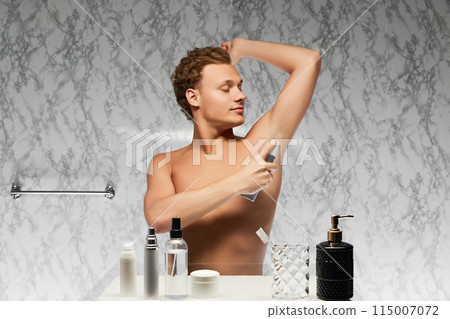 Young shirtless man use perspirant raising hand and applying it on underarm area against marbled wall in bathroom. Young shirtless man use perspirant raising hand and applying it on underarm area against marbled wall in bathroom. 115007072