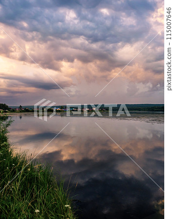 Calm river at sunset with reflective sky in rural countryside landscape Calm river at sunset with reflective sky in rural countryside landscape 115007646