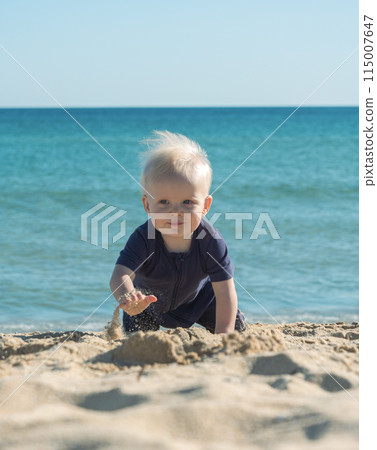 Happy blonde boy crawling on the sand near the ocean on a sunny day Happy blonde boy crawling on the sand near the ocean on a sunny day 115007647