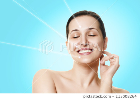 Laser facial rejuvenation. Beautiful smiling female face with closed eyes and hair up in a bun and laser rays on a gradient blue background. 115008264