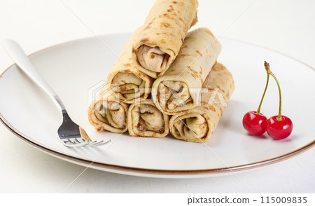 Stack of fried crepes with filling on a round plate, white table 115009835