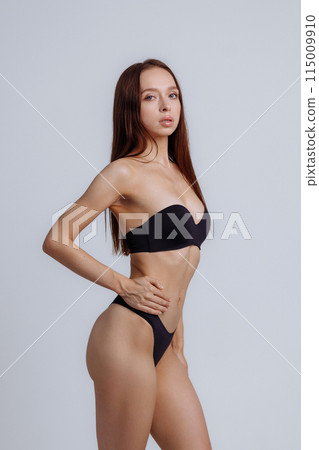 Woman model posing in black lingerie on a gray background. 115009910