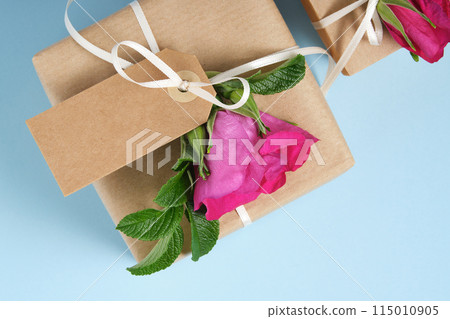 Fragment of brown gift box with blank gifttag and rosehip flowers on blue background. Space for your text 115010905