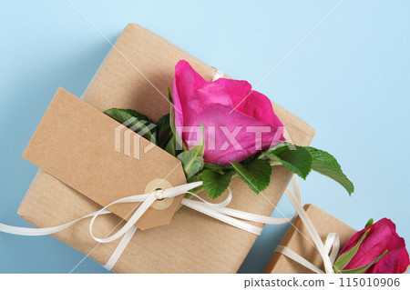 Part of brown gift box with empty label and rosehip flowers on blue background. Space for your text 115010906