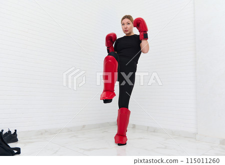 European blonde young kickboxing woman in black activewear and red kickboxing gloves, isolated on white background performing a martial arts kick. Sport exercise, fitness and cardio workout workout. 115011260