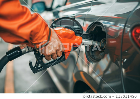 At a gas station, a person in a yellow jacket is fueling up a car using a fuel nozzle 115011456