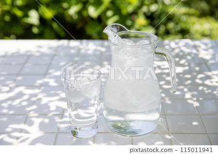 花園樹蔭下的桌子上放著水罐和冷水杯 115011941