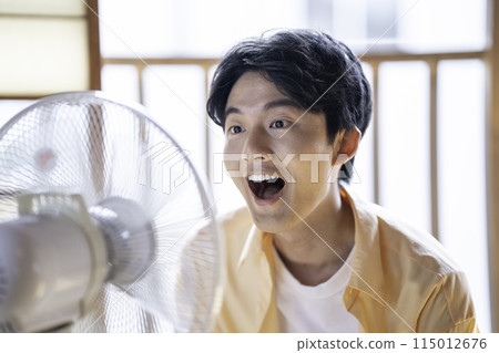 A young man cooling off with a fan A young man cooling off with a fan 115012676