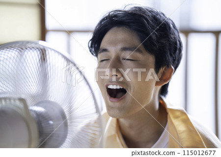 A young man cooling off with a fan A young man cooling off with a fan 115012677