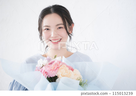 A young woman receiving a bouquet of flowers as a gift, looking at the camera A young woman receiving a bouquet of flowers as a gift, looking at the camera 115013239
