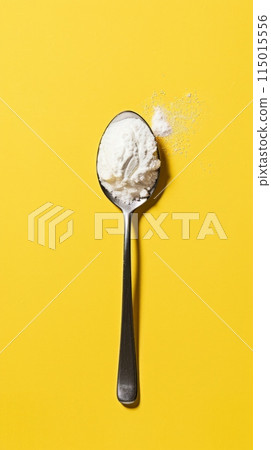 Spoon with powdered stevia against a vibrant yellow background. Healthy sugar substitutes for low-calorie diets. 115015556