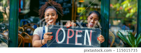 Smiling cafe staff holding a wooden 'Open' sign at the entrance. Friendly and inviting atmosphere perfect for cafes, restaurants, and local businesses. 115015735