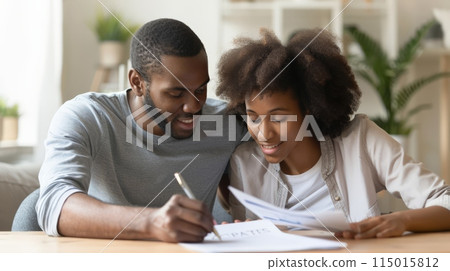 Happy African American couple reviewing mortgage documents at home. Concept of homeownership and financial planning. 115015812