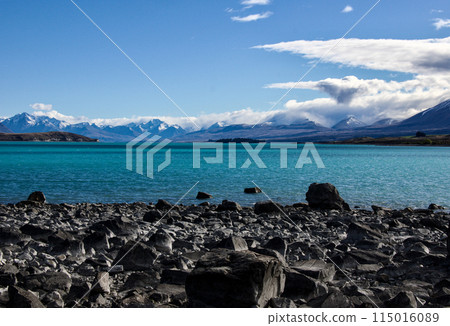Rocky shoreline of Lake Tekapo in New Zealand with the unusual coloured water in the background. The colour is created by the silt being washed down from the melting ice in the surrounding mountains.  115016089