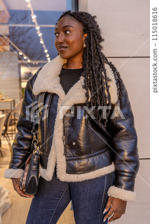 A stylish black woman in a shearling leather jacket exudes confidence and elegance 115018616