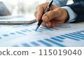 Close up of a businessman's hand holding a pen working with a financial chart and data on a desk in an office. 115019040