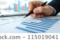 Close up of a businessman's hand holding a pen working with a financial chart and data on a desk in an office. 115019041