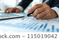 Close up of a businessman's hand holding a pen working with a financial chart and data on a desk in an office. 115019042