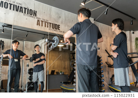 A male trainer showing a training example to members at a personal gym (arm and shoulder training) A male trainer showing a training example to members at a personal gym (arm and shoulder training) 115022931