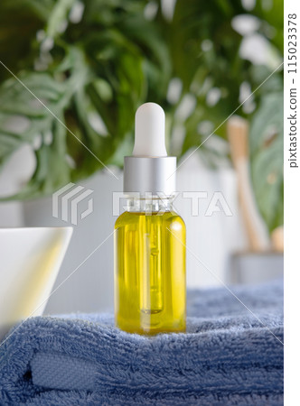 Dropper bottle filled with yellow oil on blue towel near green plant in bathroom, mockup Dropper bottle filled with yellow oil on blue towel near green plant in bathroom, mockup 115023378