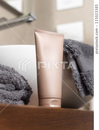 Beige cosmetic tube near grey folded towels on basin on wooden countertop in bath, mockup 115023385