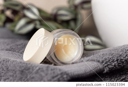 Opened lip balm jar on dark grey towels, near plant and basin on wood in bathroom, mockup 115023394