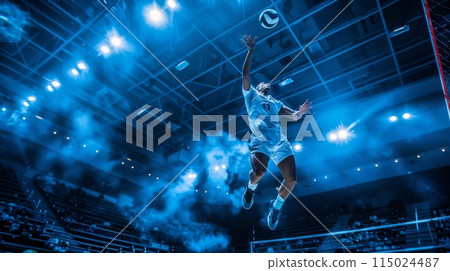 Volleyball match in a professional sports indoor court. A player in mid air about to strike the ball 115024487