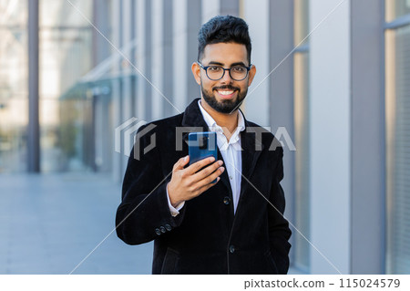 Smiling business man using smartphone typing text answering messages chatting online in city street 115024579