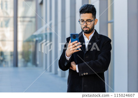Stylish business man using smartphone typing text answering messages chatting online in city street Stylish business man using smartphone typing text answering messages chatting online in city street 115024607