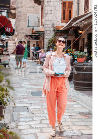Happy young Caucasian woman holds paper map in her hand, smiling and walks around an old European city for sightseeing. Summer vacation alone. Vertical orientation Happy young Caucasian woman holds paper map in her hand, smiling and walks around an old European city for sightseeing. Summer vacation alone. Vertical orientation 115024792
