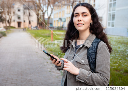Portrait of pretty young Caucasian woman looking at camera and holding phone in her hand. Concept of psychology and modern lifestyle Portrait of pretty young Caucasian woman looking at camera and holding phone in her hand. Concept of psychology and modern lifestyle 115024804