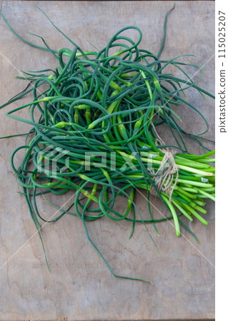 Garlic arrows. A bunch of greens on the table. Vegetable healthy vitamin food. Green stalks seedlings for salad and stewing. Vegetarianism. Garlic arrows. A bunch of greens on the table. Vegetable healthy vitamin food. Green stalks seedlings for salad and stewing. Vegetarianism. 115025207