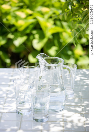 在樹蔭下的露台上，在桌子上放一個玻璃杯和水罐，保持水分充足 115025442