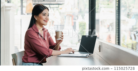A woman is sitting at a table with a laptop and a cup of coffee. She is smiling and she is enjoying her time A woman is sitting at a table with a laptop and a cup of coffee. She is smiling and she is enjoying her time 115025728