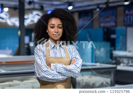 Portrait of a confident seller in the fish department at a market. The seller stands with arms crossed, wearing an apron and checkered shirt. 115025796