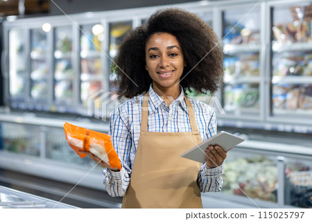 Smiling grocery store employee holding a tablet and product in the frozen food aisle, showcasing customer service and technology use in retail. Smiling grocery store employee holding a tablet and product in the frozen food aisle, showcasing customer service and technology use in retail. 115025797