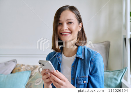 Young woman using smartphone sitting on couch at home 115026394