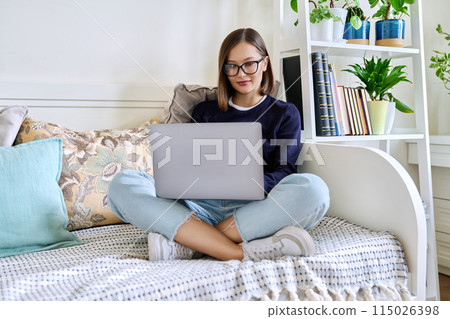 Young woman in glasses working at home, sitting on couch using laptop Young woman in glasses working at home, sitting on couch using laptop 115026398