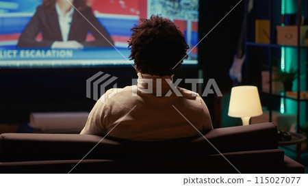 African american man watching Video on demand channel on widescreen television set in neon lit living room. Cord cutter entertained by streaming service program broadcasted on smart TV in home theatre African american man watching Video on demand channel on widescreen television set in neon lit living room. Cord cutter entertained by streaming service program broadcasted on smart TV in home theatre 115027077