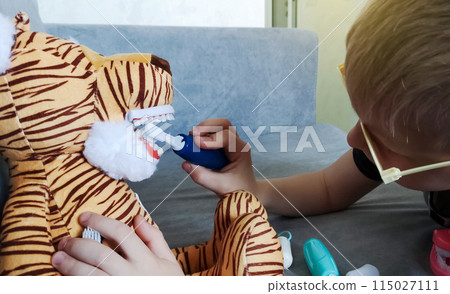 A boy brushes his teeth with a toy with an artificial jaw. Playing as a dentist, professional preparation of a child for the profession of a pediatric dentist. Hygiene and dental care 115027111